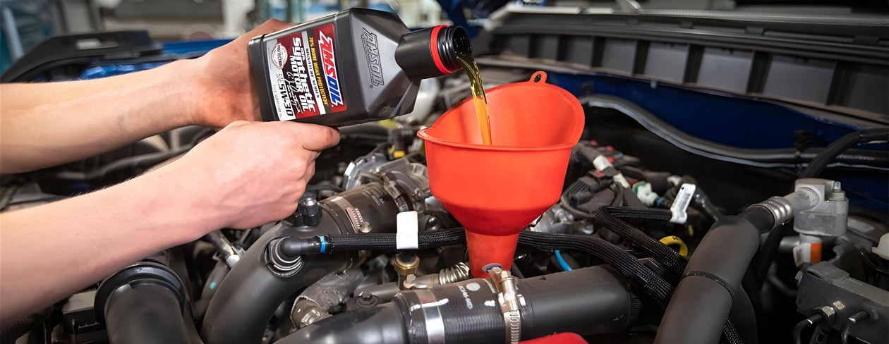 A picture of a person doing an oil change using AMSOIL 100% Synthetic motor oil, our top-tier premium engine oil.