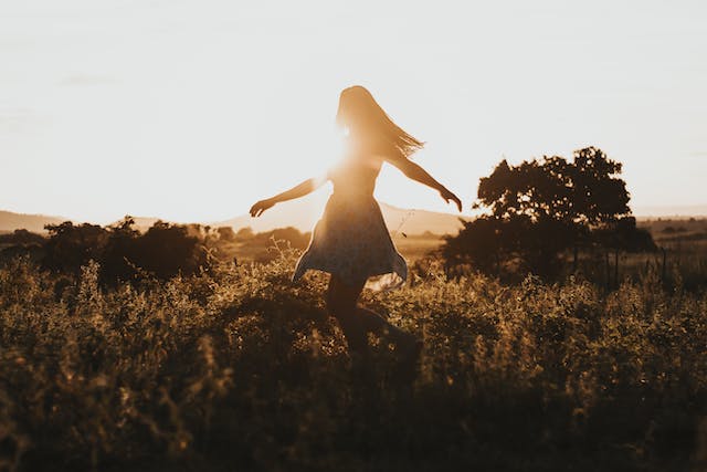 une femme tournoyant dans un champ avec le soleil en fond