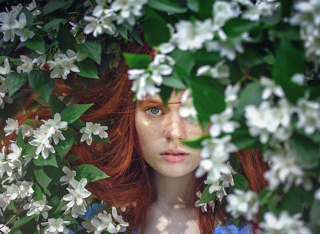 une femme rousse caché par des fleurs blanches