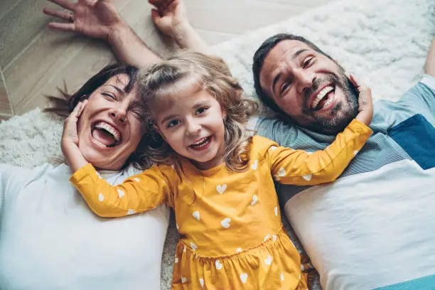 un couple avec leur petite fille allongés sur le sol en riant