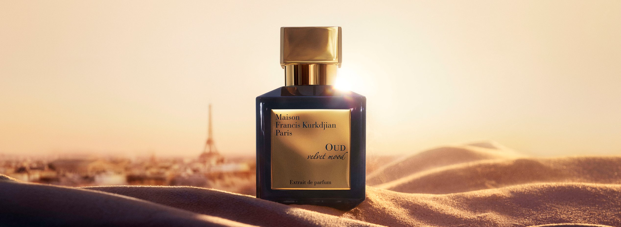 Maison Francis Kurkdjian OUD velvet mood Extrait de Parfum bottle on desert sand dunes with the Eiffel Tower at golden hour