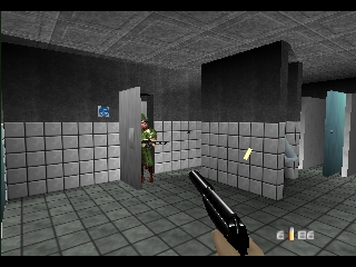 A first-person perspective shows a player character with an assault rifle in a tiled interior room with white and gray checkered walls. A yellow-suited figure stands in the middle distance near gray pillars and a large black rectangular structure. A blue cylindrical object is visible on the right side. The HUD displays ammo count and weapon information in the lower right corner. The scene uses low-polygon 3D graphics typical of N64-era games, with flat-shaded surfaces and a gray concrete ceiling.