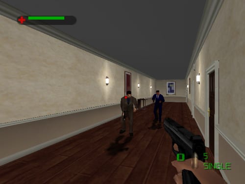 A first-person perspective corridor with two armed figures standing in the distance. The player's weapon is visible in the lower right corner. A green health bar appears in the upper left, and HUD elements show weapon ammo and status at the bottom right. The hallway features beige walls with sconce lighting, a dark wooden floor, framed artwork, and doors on either side. The ceiling is dark gray.