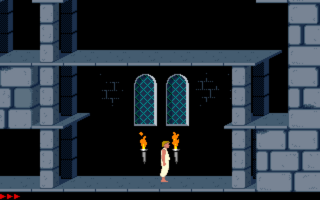 A stone chamber interior displays two tall arched windows with teal-green lattice panes in the center background. Two orange flames flank a white figure standing beneath the windows against a black interior wall. Gray brick pillars frame the left and right edges, with darker stone passages visible at top corners. The scene uses a limited palette of grays, blacks, oranges, and teals typical of early DOS-era pixel graphics.