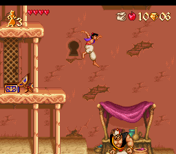 Aladdin stands on a tan platform in the center-right of the screen, facing left with his arm raised. A purple canopy tent occupies the lower-right corner. Brown rocky terrain and scattered boulders fill the background. The left side shows a wooden structure with latticed details and a doorway. A health meter displays four red hearts in the upper-left corner, with a score counter showing 10 and 06 in the upper-right. The sprite animation shows 16-bit pixel art rendered in warm brown and orange tones against an earthy background.