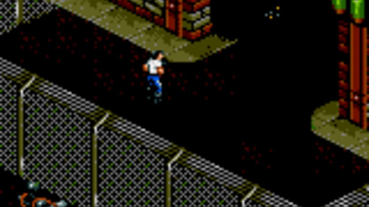 A character in white shirt and blue pants stands in the center of an isometric maze environment with yellow-green checkered floor tiles and black walls. Chain-link fencing lines the lower left area, while red brick structures appear in the upper right corner. The scene uses a limited 8-bit color palette with black background space dominating the composition. Scattered red pixels suggest enemies or hazards throughout the maze area.