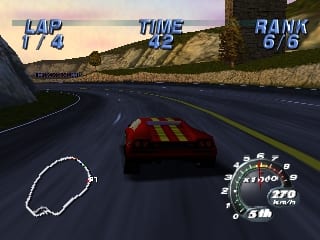 A red Lamborghini sports car drives on an asphalt road through a mountainous landscape with brown rocky cliffs visible on both sides. The car is centered in the view with a white track outline visible ahead. The top of the screen displays blue UI text reading "LAP", "TIME", and "RANK" with numerical values. The bottom right corner shows a circular speedometer gauge with MPH markings and a digital speed readout. The sky features a gradient from orange to blue, indicating sunset or sunrise lighting. The road stretches into the distance with a slight curve.