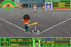 A young baseball player in an orange and black uniform stands at bat on a diamond field during daytime. The batter faces right, holding the bat in ready position. At the top of the screen, a horizontal HUD displays the game interface with team logos, player status information, and innings/score readout across green and tan panels. The left sidebar shows additional game stats and player details in yellow and green text boxes. The background shows a residential street with buildings and trees rendered in flat, sprite-based graphics typical of Game Boy Advance sports games.