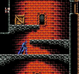 Batman stands on a gray stone platform in the lower-left portion of the screen, rendered as a blue-suited sprite with red cape. A red brick wall dominates the background with a dark window opening in the upper-middle section. Gray stone platforms form a descending staircase pattern across the screen. Black areas represent empty space or shadows. A vertical gold-colored border frames the right edge of the play area. The NES game uses a limited color palette of red, blue, gray, black, and gold with typical 8-bit sprite pixelation.