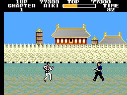 A martial arts fighter in white gi stands in shallow water facing a black-clad opponent on a beach. Behind them sits an ornate Asian temple structure with red and gold roofing and cream-colored stone walls. The top of the screen displays a score panel reading "TOP CHAPTER," "POWER," "AIKI," and "TOP" with numerical values. The scene uses a limited color palette of blues, greens, golds, and earth tones typical of early 8-bit SMS graphics, with visible pixelated sprites and a flat parallax background.