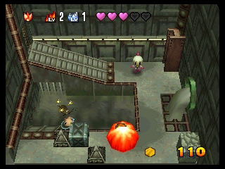 A top-down isometric game view shows Bomberman standing in the lower-left area of a tiled arena with brown brick walls forming a maze layout. A large orange explosion effect dominates the center-right of the screen. The UI displays health hearts in the top-left corner, a score of 110 in the bottom-right, and an overhead minimap. Gray stone floors and wooden crate obstacles fill the playable space, with a small pink character visible in the upper portion of the arena.