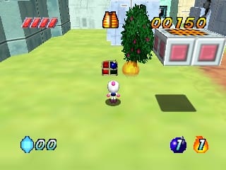 A white bomberman character stands in the center of a bright green arena, surrounded by destructible crates and environmental obstacles. A potted green plant grows behind the character. The top-left corner displays red damage indicators and a blue health counter showing 00. The top-right shows a gold score of 00160 and numbered circular UI elements. Two rounded white structures with pink-red panels sit in the background. The scene uses a 3D polygonal art style with flat-shaded surfaces typical of N64 graphics, rendering the level in isometric perspective.