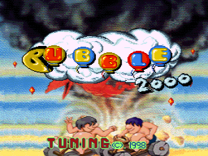 The title screen features a large red airship or zeppelin sprite in the center with five colorful bubble characters arranged across its top section. Below the airship, two characters stand on a beach with blue water and yellow sand visible in the background. The text "TUNING" and "1998" appears at the bottom, with small red and blue dot sprites scattered throughout the composition. The overall art style uses bright colors and low-resolution sprite graphics typical of late-1990s arcade games.