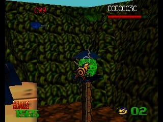 A green bee character hovers centrally in a dense forest environment with dark foliage filling the background. Wooden crates and platforms appear in the lower left corner. The UI displays a red health bar in the upper right, a score counter showing 02 in the lower right, and numerical indicators at the top left. The 3D graphics use a low-polygon style typical of N64 games, with a limited color palette dominated by greens and browns for the forest setting.