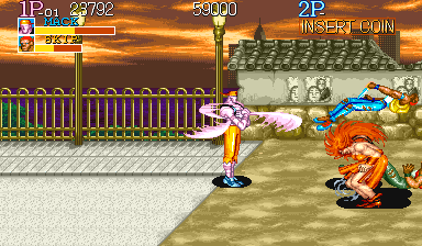 A two-player arcade scene displays a character in white and pink clothing performing a kick attack against an orange enemy on a dirt ground. A purple fence and stone wall structure occupy the background. The top HUD shows Player 1 score of 29792, Player 2 label with INSERTED COIN, and a small life meter. Yellow and blue UI elements appear in the upper left corner. The sprite style uses bright colors with defined pixel outlines typical of early 1990s arcade graphics.