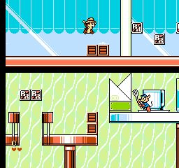 A split-screen level layout shows two connected rooms with 8-bit sprite graphics. The upper room features a small character sprite near the top left, wooden crate blocks in the center, and a light blue floor against a blue striped wall background. The lower room displays a larger green-tiled floor with diagonal line patterns, various colored block platforms in red and yellow, and a character sprite operating machinery on the right side. White vertical pipes and structural elements divide the spaces, and small numeric UI elements appear in corners, typical of NES-era platformer level design.