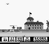 A monochromatic Game Boy screenshot displays a pixelated military compound or fortification with a tall central tower flying a flag, surrounded by defensive structures and walls. A small helicopter sprite appears in the upper-left airspace. The bottom of the screen shows a black UI bar containing what appears to be a score display reading "15 68 1 63 SCORE" with pixel-based numerals. The overall scene uses the Game Boy's typical four-shade grayscale palette with blocky sprite work characteristic of early handheld gaming.
