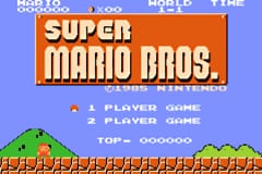 The title screen displays 'SUPER MARIO BROS.' in large orange text against a blue background. Below the logo are two menu options: '1 PLAYER GAME' and '2 PLAYER GAME'. The bottom third shows a pixelated side-scrolling level with green grass, brown brick platforms, and red question mark blocks typical of the NES art style. A small red character sprite and coin sprite are visible in the upper left corner. The entire interface uses low-resolution sprites and a limited color palette characteristic of Game Boy Advance graphics.