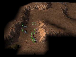 An isometric tactical view shows a brown desert terrain with scattered rocky outcroppings and shadows. Small green units and structures dot the landscape, positioned across the uneven ground. The camera angle reveals the 3D terrain with visible elevation changes and darker shadowed areas on the northern side. The sprite-based graphics display units at a small scale typical of late-1990s console strategy games, with limited color palette emphasizing browns, greens, and grays against the black background.