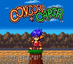 The title screen displays "Congo's Caper" in large colorful lettering at the top, with orange and green text against a bright blue sky. Below, a small sprite character with purple hair and red clothing stands on brown terrain with scattered rocks. A dense forest of dark trees fills the background, with white clouds visible in the upper portion. Yellow-brown ground and sparse vegetation occupy the lower third. White text reading "PUSH START BUTTON" appears centered near the bottom of the screen.