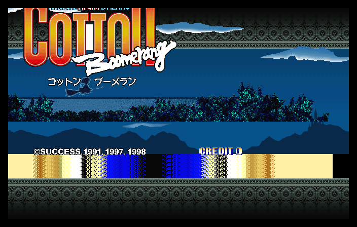 The arcade title screen displays 'Cotton Boomerang' in large orange and red letters at the top, with Japanese characters below. A stylized white boomerang graphic curves across the logo. The background shows a blue water scene with layered parallax mountains and tree silhouettes in varying shades of blue and teal. A decorative gray ornamental border frames the top and bottom. Copyright text reads '©SUCCESS.1991.1997.1998' on the lower left with 'CREDIT 0' on the right. A yellow-beige horizontal bar with blue pixelated patterns spans the bottom section, typical of arcade cabinet aesthetics.