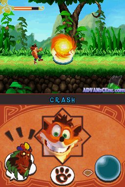 A split-screen layout showing Crash Bandicoot gameplay above and a character select or status menu below. The upper screen depicts Crash running left through a jungle level with green grass, large plants, and a large tree in the background, while a golden fireball projectile explodes in front of him. A health bar and score counter appear in the top-left. The lower screen displays Crash's face in a large circular portrait with an orange decorative border featuring geometric patterns, flanked by small icons including what appears to a power-up indicator on the left and a dark circular button on the right.