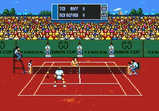A tennis match in progress on a red clay court with white boundary lines. Two players are positioned on opposite sides of the net, with one preparing to serve. A crowd of orange and yellow spectators fills the stadium stands in the background beneath a blue sky. A scoreboard at the top displays "TOP RUFF 0" and "RAD MERAD 0" in white text on a blue background. The Davis Cup logo and "TENGEN" branding are visible on signage around the court perimeter. Sprite-based graphics render the players, ball, and court details in the characteristic pixelated style of early Sega Genesis sports titles.