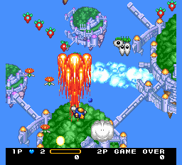 A vertical-scrolling shooter displays a bright blue sky with a large red laser beam firing downward from the player's ship at center. Colorful enemy formations scatter across the upper screen, while green terrain and gray structures line the left and right edges. A score panel at the bottom shows 1P and 2P indicators with health bars and "GAME OVER" text. Pixel-based sprites and cloud formations create a compact, vibrant isometric perspective typical of early 1990s PCE arcade ports.