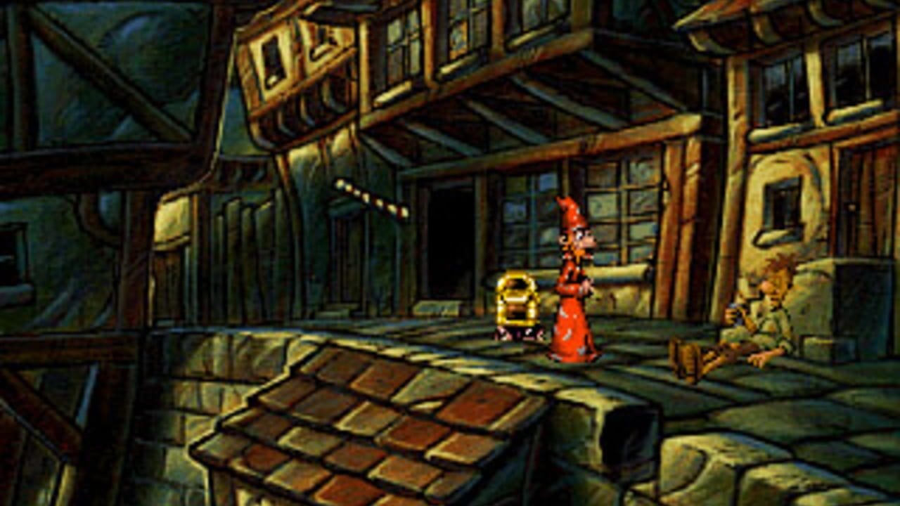 A medieval tavern interior with wooden beams and lanterns overhead. A character in a red pointed hat stands center-stage next to a yellow-robed figure. To the right, another character sits on a bench. The floor features brown brick paving, and the scene uses a limited color palette with warm yellows, greens, and browns typical of early 1990s pixel art. Wooden architectural elements frame the scene, with lantern light creating shadows on walls and doorways visible in the background.