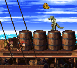 A Kong character stands on a wooden ship deck atop four brown barrels arranged in a row, with ship rigging visible above and a blue sky with clouds in the background. A volleyball floats in the upper portion of the screen. The scene displays the SNES-era pixel art style characteristic of the platform, with a side-scrolling perspective showing the deck environment and tropical setting.