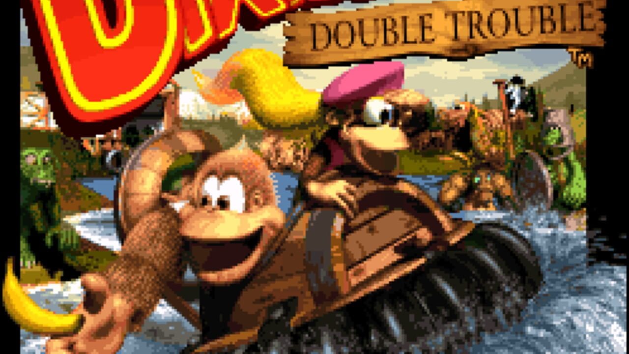 Two brown gorilla characters stand prominently in the foreground against a riverside landscape with green vegetation and mountains. The character on the left holds a banana, while the one on the right wears a burgundy cap. A red neon-style logo appears in the upper left corner, with a wooden "DOUBLE TROUBLE" banner visible at top right. The background shows additional characters and structures along the waterside, rendered in colorful SNES-era pixel art with a warm brown and green color palette. The scene depicts a lush jungle environment with parallax layering in the distance.