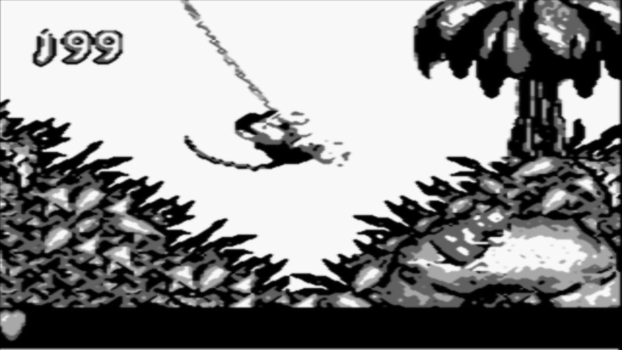 A monkey character mid-jump swings across a gap between two spiky vine-covered platforms in this black and white Game Boy screenshot. The playable character is suspended on a rope in the center of the screen against a light background. Jagged, dark spikes cover both the left and right cliff faces, with gray rocky terrain visible at the base. A dark structure or tower appears in the upper right. The score display shows 0099 in the top left corner. The art style uses limited grayscale sprites and pixel-based graphics typical of Game Boy hardware.