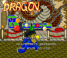 The title screen displays "DRAGON BOWL" in large orange text at the top. Below is a cartoon illustration of a colorful train with multiple cars carrying passengers and cargo, set against a background with brick patterns and clouds. A large dragon figure looms above the train on the left side. At the bottom, white text reads "©1992 NICS" and "ALL RIGHTS RESERVED" with "1992 NICS CO.LTD" below. The art style uses bright primary colors typical of early 1990s arcade graphics with low-resolution pixel sprites and hand-drawn character illustrations.