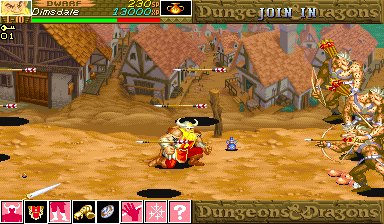 A fantasy village scene with tan-colored buildings and wooden structures arranged on a sandy ground. A player character in red armor sits centrally on the screen, surrounded by scattered items and loot. The top UI displays health bars, inventory icons in a pink row at bottom showing weapons and items, and character portraits. The right side shows a tall gold dragon statue or decoration. The sprite-based graphics use a warm brown and tan color palette with visible pixelation typical of mid-1990s arcade hardware.