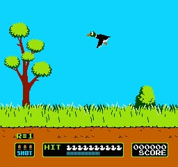 A bright cyan sky fills the upper half above a landscape with a red-trunked tree bearing four yellow flower clusters on the left, green grass in the middle ground, and brown earth at the bottom. A black bird sprite flies mid-screen to the right. The bottom UI strip displays a score counter on the left reading 0, a horizontal ammunition/ammo counter in the center showing multiple white dots, and a circular ammo count display on the right showing white circles, all rendered in pixelated NES-era graphics.