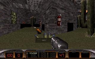 A first-person shooter view shows a player character wielding a rifle in a brick-walled outdoor arena. Stone structures with windows and doorways line the background, while a lantern-style light fixture hangs on the right wall. The ground is covered in grass. A detailed HUD spans the bottom of the screen, displaying ammo counts, health status, weapons inventory across multiple panels in brown and tan colors, typical of early 1990s DOS-era FPS design. The overall visual style uses low-resolution pixelated graphics with earthy textures.
