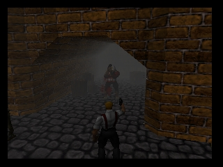 A first-person perspective view through a brick archway onto a stone-tiled courtyard. The player character's weapon is visible in the lower-right corner. A humanoid figure stands in the distance within the archway, shrouded in fog or darkness. The brick walls display brown and tan coloring with visible stone texture. The courtyard floor features a repeating checkered pattern of gray and darker stone tiles. The overall lighting is dim and atmospheric, with the distant figure partially obscured by environmental haze.