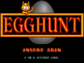 The title screen displays "EGGHUNT" in large orange letters within a rectangular border, centered horizontally. Above the text sits a cartoon orange cat character with pointed ears in the upper left, and a gray spherical object to its right. Below the title, yellow text reads "INSERT COIN" followed by "© VE-X OCTOBER 1986" in smaller orange pixelated font. The background is solid black. The overall aesthetic employs a typical arcade cabinet style with bold lettering and simple 8-bit era graphics.
