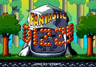 The title screen displays a large cauldron or pot with an orange spherical object (likely a collectible) on top, centered against a forest background of green trees and yellow tree trunks. The word "FANTASTIC" in orange and yellow lettering appears above the cauldron. Orange circular objects fill the interior of the cauldron, arranged in a grid pattern. The bottom of the screen shows "PRESS START" in white text. The art style uses 16-bit pixel sprites with a bright color palette typical of early 1990s Sega Genesis games.