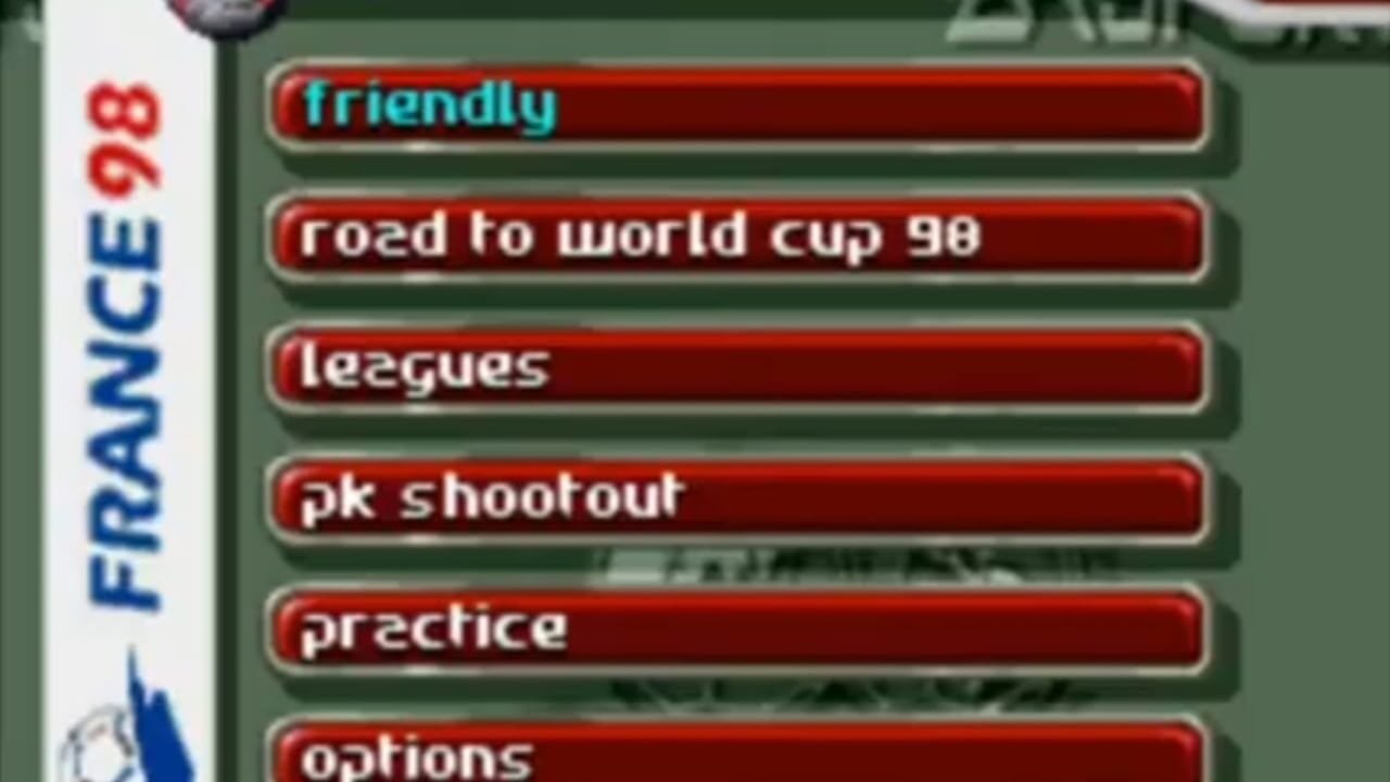 A menu screen displays six red button options vertically stacked on a green background: friendly, road to world cup 98, leagues, pk shootout, practice, and options. The Game Boy Advance logo appears on the left side, with a small FIFA 98 branding indicator above it.