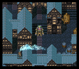 A top-down dungeon view shows a character sprite in the center surrounded by blue stone walls and dark wooden structures. The architecture features peaked roofs, narrow corridors, and brown wooden platforms arranged in a symmetrical pattern. A bright cyan explosion or magical effect emanates from the character's position. The tileset uses a 16-bit pixel art style with a blue and brown color palette, typical of SNES-era RPG dungeon design. Small doorways and passages are visible throughout the stone layout.