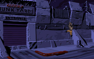 A nighttime industrial junkyard scene rendered in LucasArts' characteristic hand-painted style. Stacked metal containers and shipping crates occupy the upper portion in shades of blue and purple. A sign reading 'JUNK YARD' and 'ENTRANCE' appears on the left side. A figure in orange-red clothing lies prone on the ground in the center-right foreground, suggesting action or conflict. The color palette emphasizes cool tones with strong shadows, creating a gritty, noir-influenced atmosphere typical of the game's visual design.
