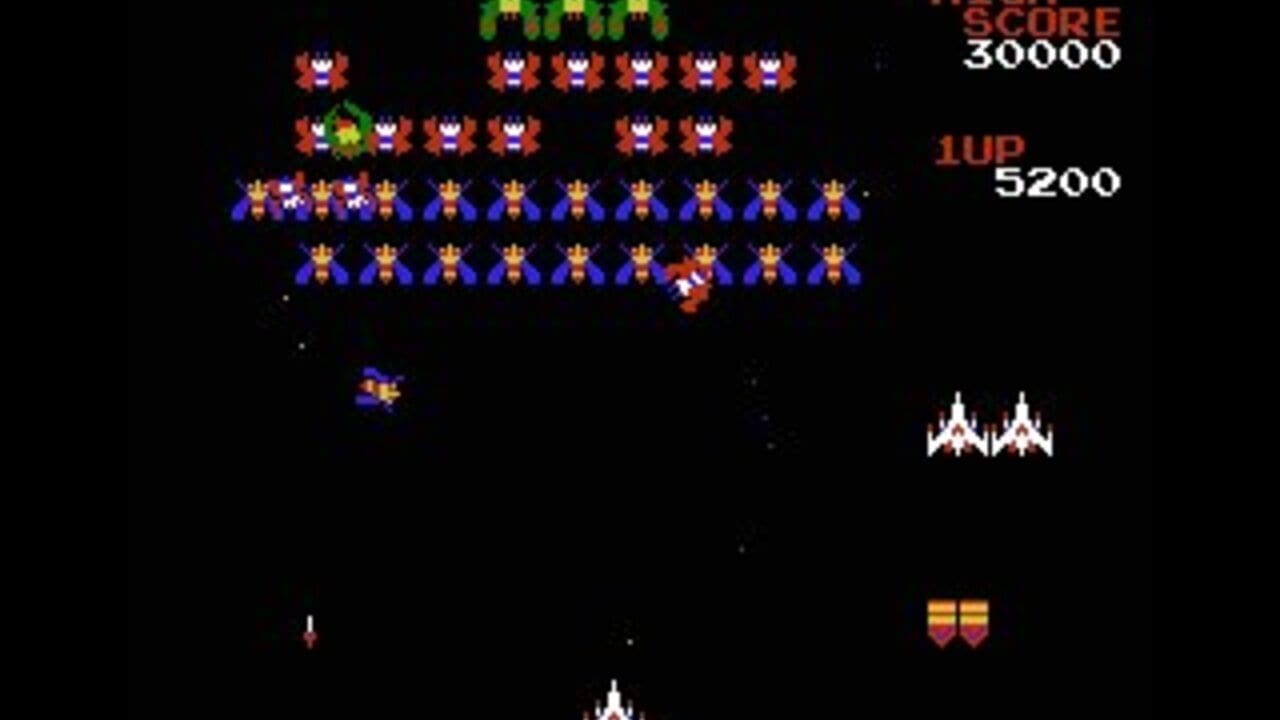 Multiple rows of blue and orange alien enemies with yellow accents fill the upper half of the screen against a black background. A red player ship positioned at the bottom center fires white projectiles upward. Green enemies appear at the very top, with two red enemy formations in the upper-left area. A white enemy formation is visible on the right side. The score display reads 30000 in the top-right corner, with 1UP and 5200 shown below. Two yellow shield indicators appear in the lower-right. Small white dots scattered across the playfield represent stars or bullet sprites.