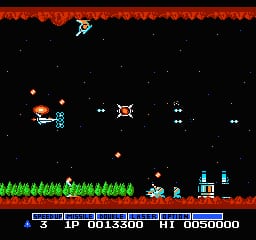 A horizontal-scrolling shooter displays a spaceship on the left side firing projectiles at multiple enemies scattered across the black starfield. The top and bottom edges show orange lava or energy barriers with a red hue. Green grass or vegetation textures appear along the bottom edge above the lower barrier. A blue building structure sits in the lower-right corner. The HUD displays a score of 0013300, remaining lives marked as 3, and high score 0050000 in white text at the bottom. Small orange and white enemy sprites occupy the mid-screen area, with various projectiles visible in flight. The entire scene uses limited 8-bit color palette typical of NES-era graphics.