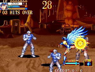 A side-scrolling beat-em-up arcade screen displays two blue-armored player characters facing a large yellow-winged enemy with spikes in a brown stone arena. The upper left shows "08 HITS OVER" with a hit counter. The top center displays "28" in yellow text. A health bar appears above the enemy, and game UI elements including score and credits line the bottom of the screen. Sprite-based 16-bit art style with warm-toned background architecture visible behind the action.