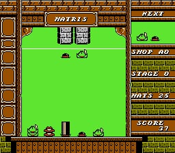 A gameplay screen displays a large green play field bordered by brick-textured walls. Two rows of falling hat sprites appear in the upper-center area, with additional hat pieces visible near the bottom left. The right side shows a control panel with brown brick pattern containing text labels for NEXT, SHOP, ROWS, PUTS, and SCORE with corresponding numerical displays. The interface uses a limited 8-bit color palette with orange, green, brown, and black tones typical of early 1990s NES graphics.