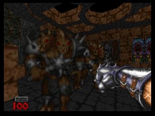 A first-person view shows a player character holding a glowing silver weapon in the foreground, aiming at two demonic gray enemies in a stone brick corridor. The environment features ornate brown wooden decorative elements on the walls above, torches providing warm light, and a health/mana UI bar in the lower left corner. The enemies display a dark, grotesque appearance characteristic of early 3D polygon modeling with visible blocky geometry.