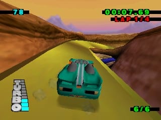 A green Hot Wheels car viewed from behind drives on a bright yellow track cutting through a desert landscape with brown rocky terrain. Mountains appear in the distance under an orange-tinted sky. The track is elevated above the surrounding area. HUD elements display in the top-left corner with a small map, top-right shows a score counter reading 00207-50, and bottom-left contains controller button icons. Another blue car is visible ahead on the track in the distance.