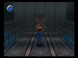 A character in brown and blue clothing stands centered on metal grating with two parallel rails stretching into the distance. The industrial corridor is flanked by blue metal railings on both sides. Dark textured walls with vertical panels form the background. A blue power icon appears in the top-left corner of the screen. The low-polygon 3D graphics typical of N64-era games are visible throughout the scene.
