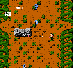 A top-down view of a military jeep centered on an orange sandy terrain dotted with small green vegetation patches. The jeep is white with dark detailing and appears to be the player-controlled vehicle. Multiple enemy soldiers in blue uniforms are scattered across the landscape at various distances. The screen edges show dense green foliage or jungle terrain forming natural borders. The 8-bit sprite style and orange-brown color palette are characteristic of NES-era graphics, with the HUD displaying "500" in the upper-left corner indicating the current score.